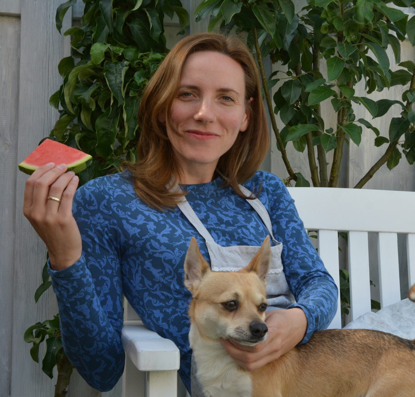 Frau mit Wassermelonen-Stück und Hund auf der weißen Gartenbank
